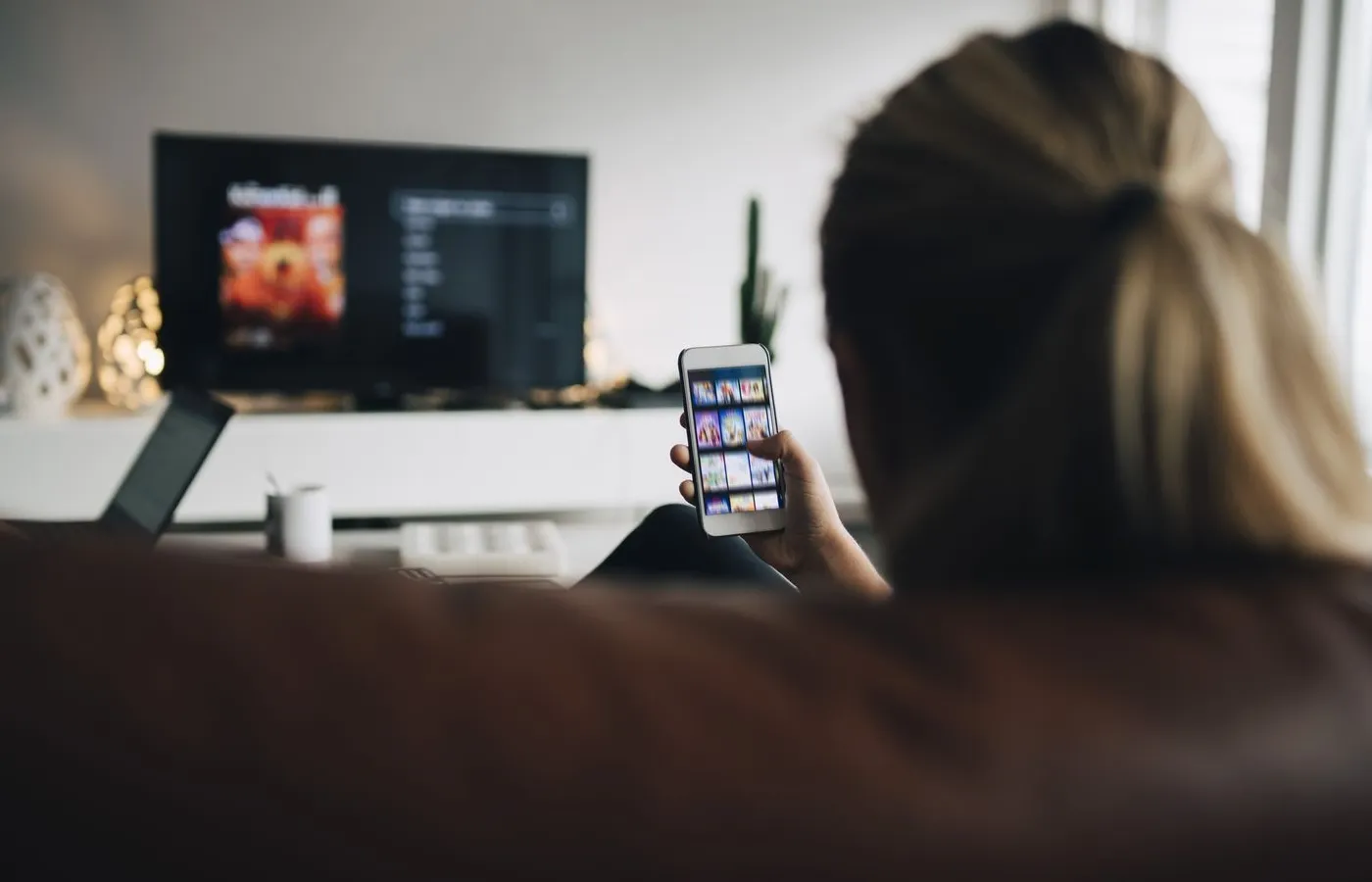 Orang menggunakan smartphone sambil menonton TV di ruang keluarga