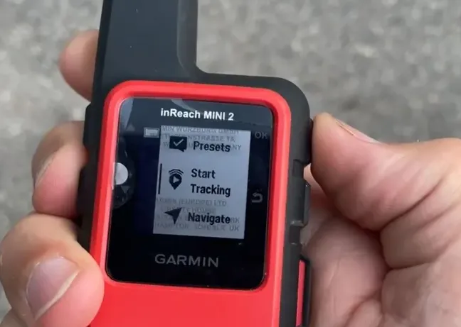 Hand holding small black and red satellite messenger device with antenna and screen