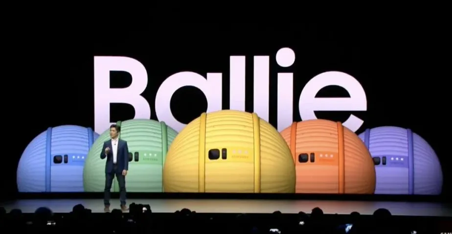 Robot bola kecil berwarna kuning Samsung Ballie di atas lantai kayu dengan latar belakang buram