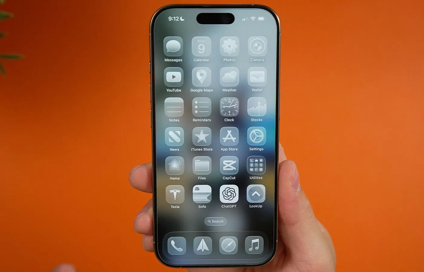 Tangan memegang iPhone menampilkan antarmuka mode gelap dengan latar belakang oranye