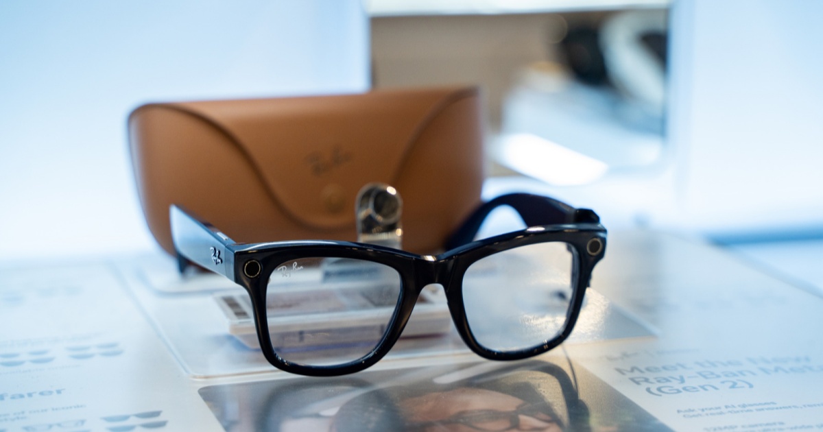 Sepasang kacamata pintar Ray-Ban Meta yang dipajang di atas meja dengan latar belakang ruangan modern.