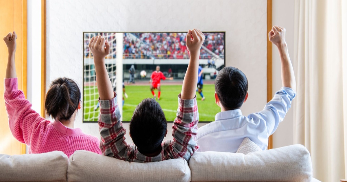 Keluarga menonton pertandingan sepak bola di TV 4K sambil bersorak gembira di ruang tamu