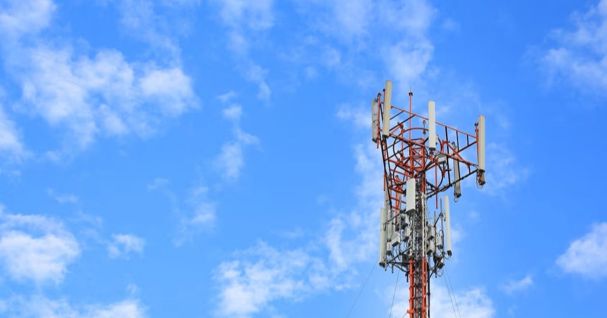 Ilustrasi menara seluler dengan latar langit biru, melambangkan infrastruktur telekomunikasi yang terkena dampak kenaikan harga chip.