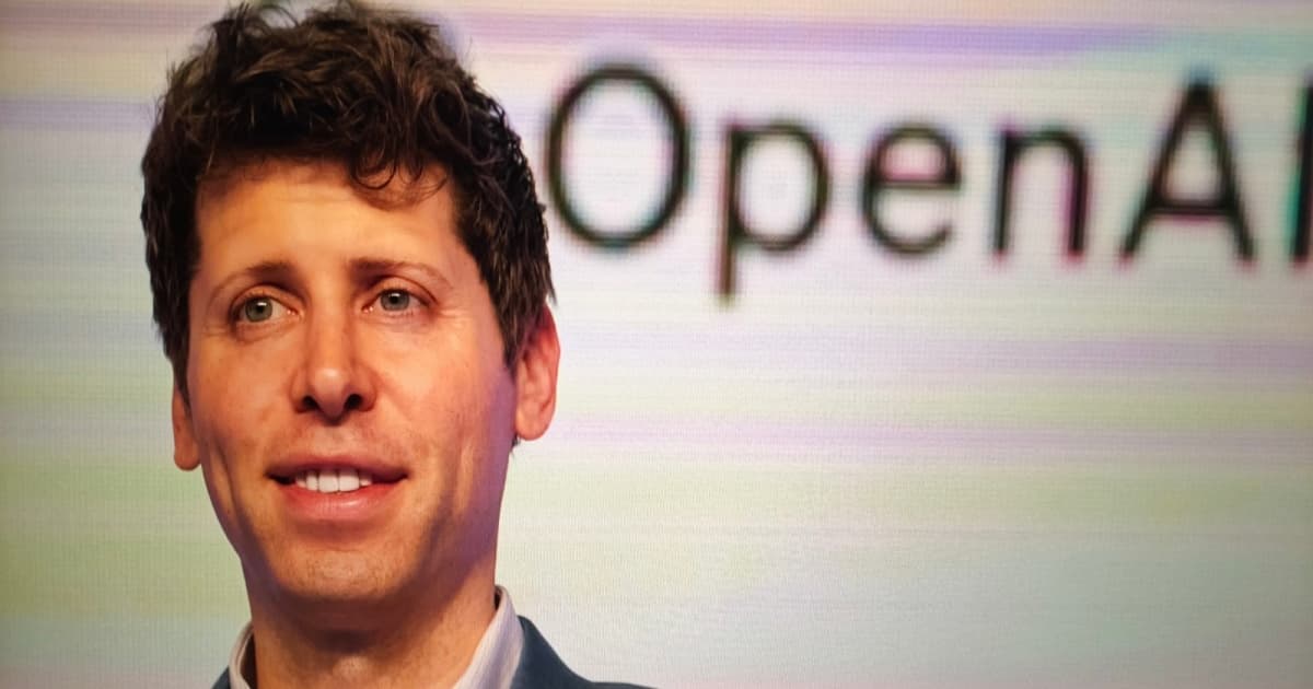 Seorang pria berdiri di depan logo OpenAI berwarna hijau dengan latar belakang gelap