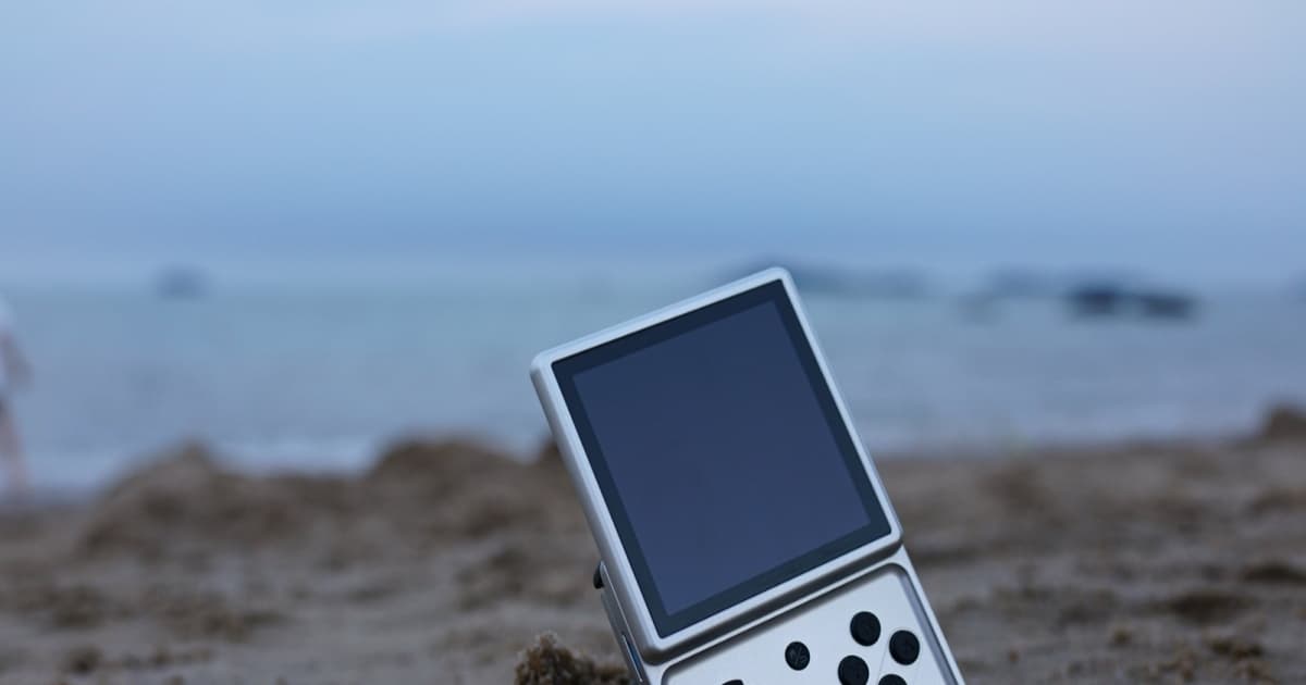 Anbernic RG Rotate di atas pasir dengan latar belakang pantai