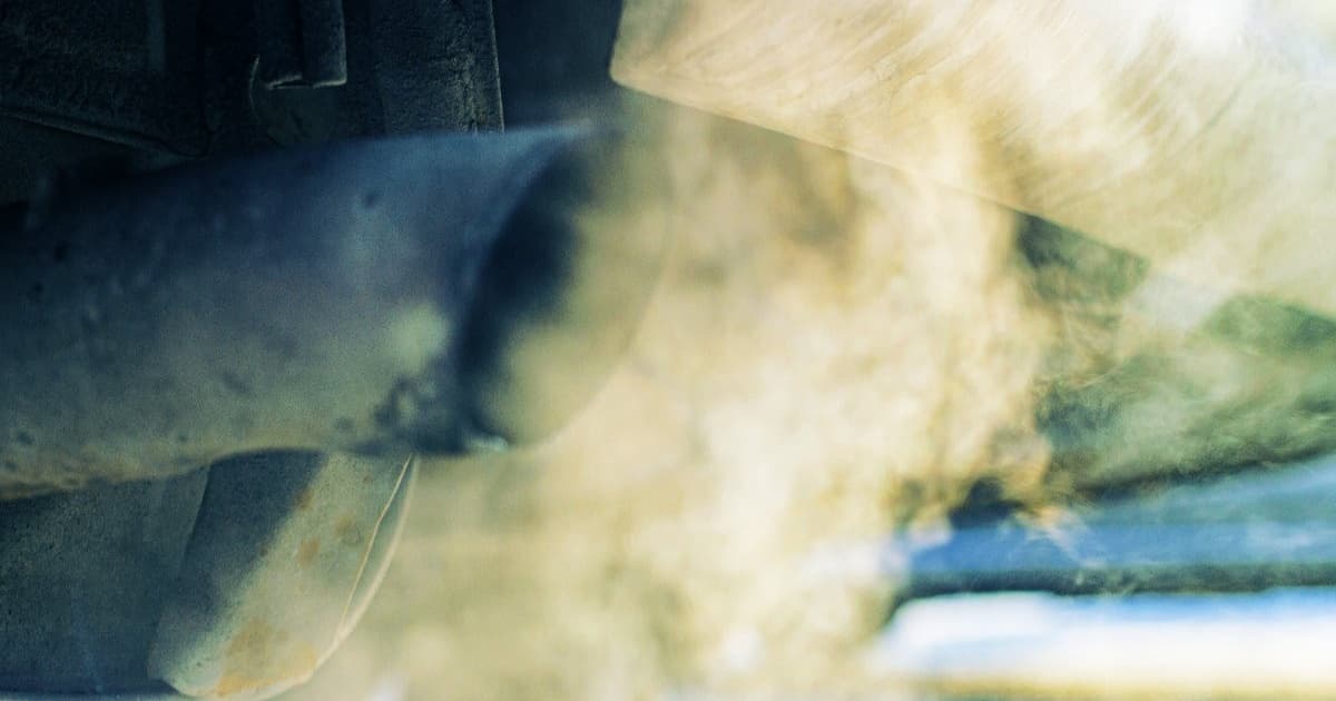 Close-up knalpot mobil bensin yang mengeluarkan emisi