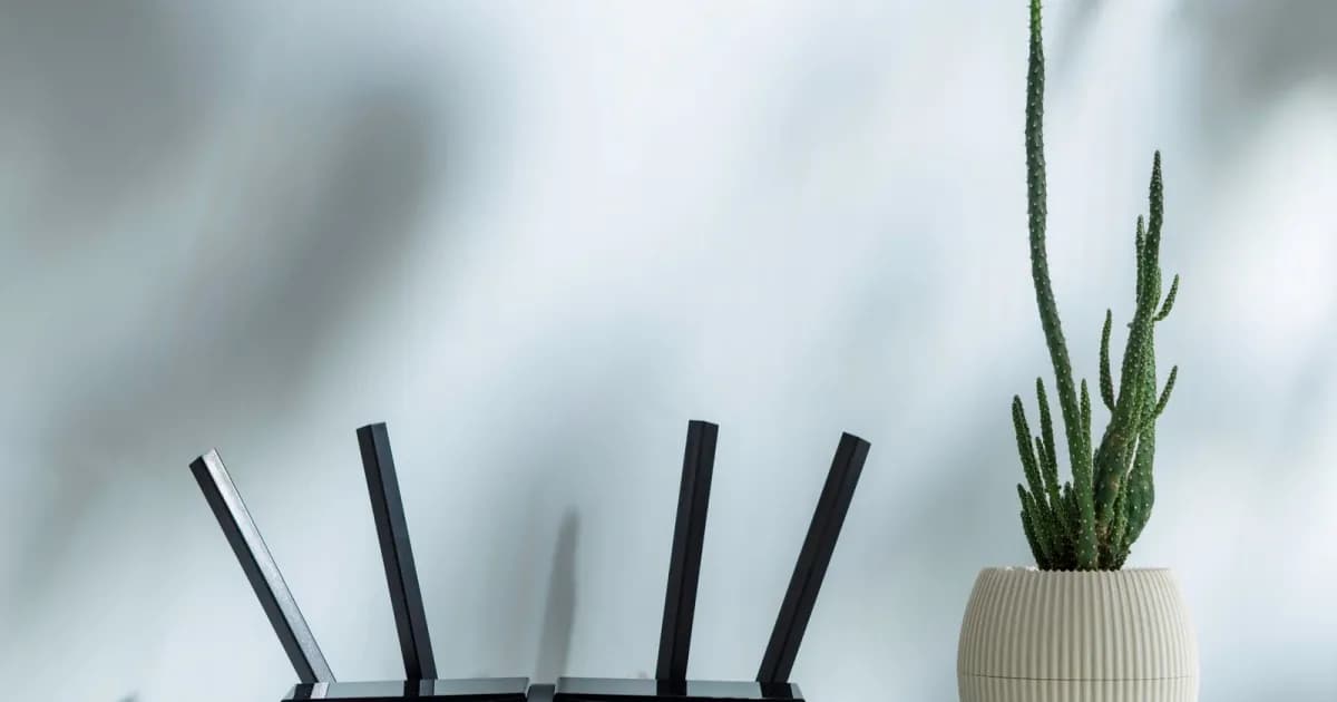 Router hitam dengan empat antena di atas meja dengan kaktus pot di dekatnya
