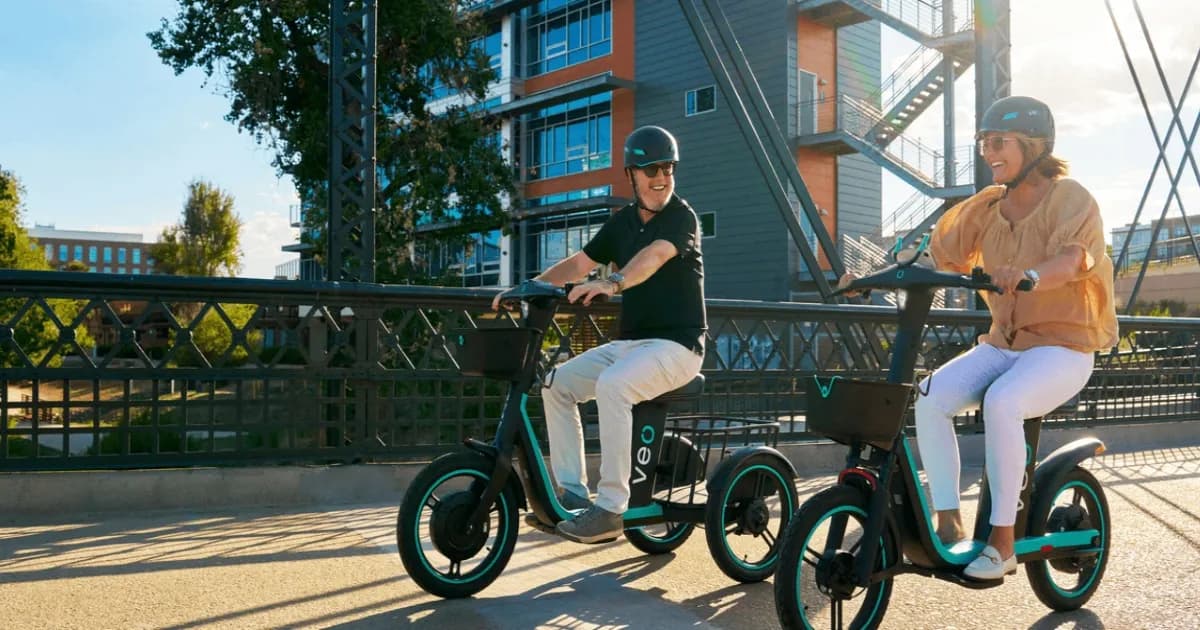 Veo Rover skuter listrik roda tiga berwarna orange diparkir di trotoar dengan latar belakang kota Denver