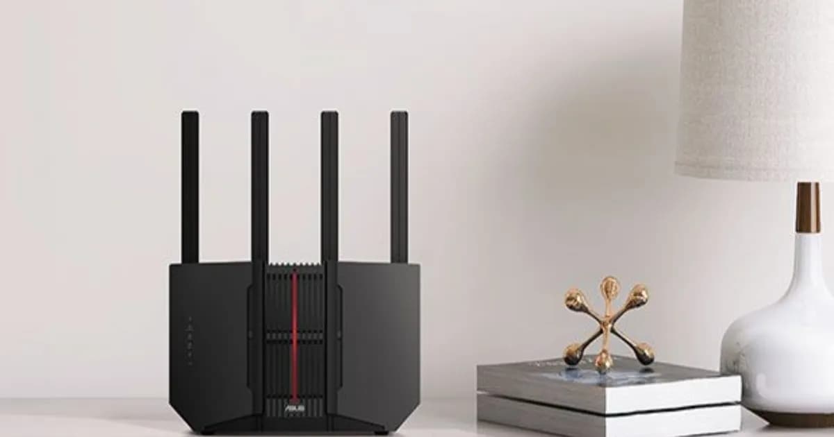 Router Asus RT-BE92U dengan empat antena di atas meja kayu, berdampingan dengan lampu dan buku