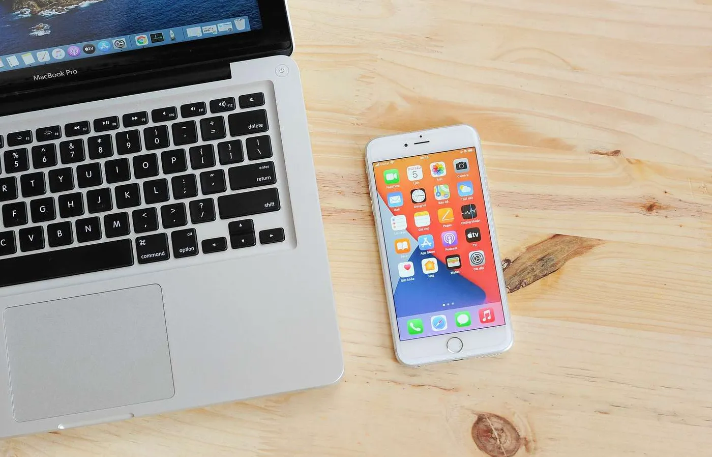 Laptop MacBook Air dan smartphone iPhone yang diletakkan di atas permukaan kayu dengan layar terbuka