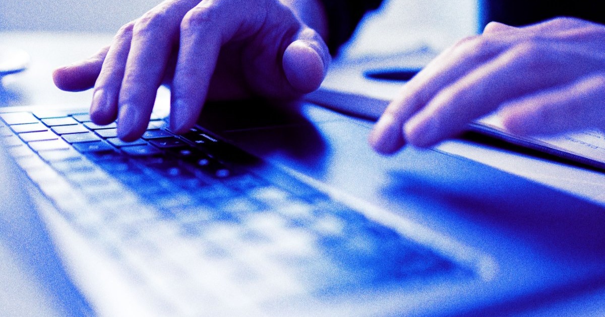 Tangan mengetik di laptop dengan efek pencahayaan biru, fokus pada jari yang menekan keyboard