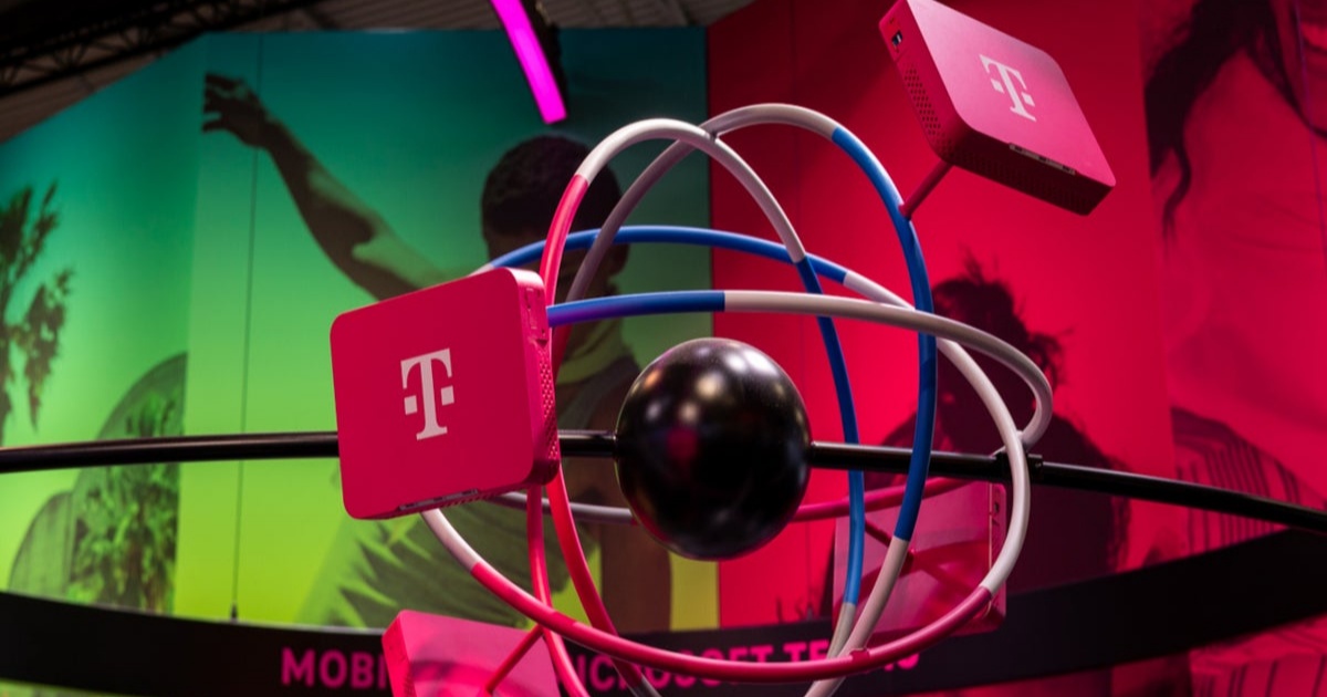 Seorang tenaga penjualan T-Mobile menunjukkan aplikasi T-Life di ponsel kepada pelanggan di dalam toko.