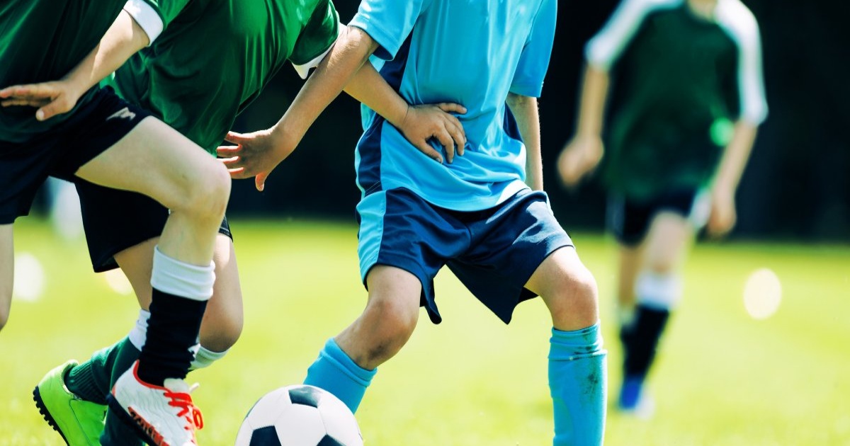 Anak-anak bermain sepak bola di lapangan hijau