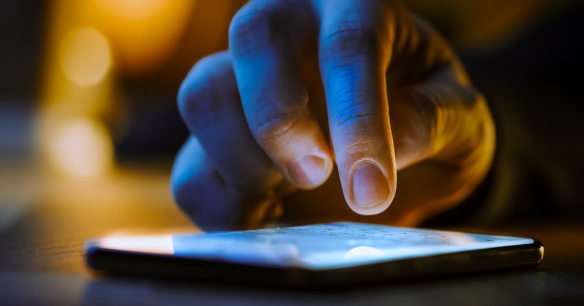 Tangan mendekati layar ponsel yang menyala dengan latar gelap