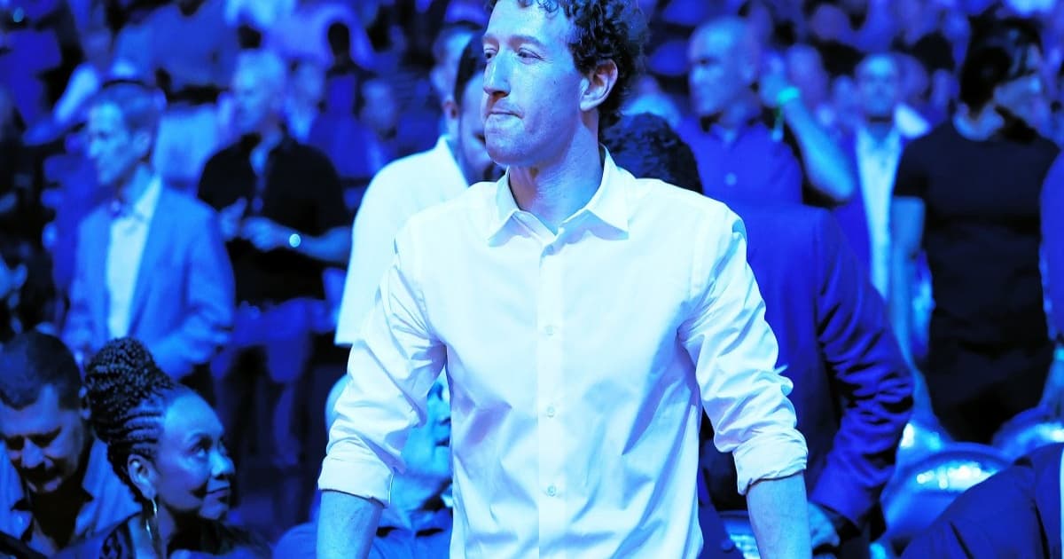 Mark Zuckerberg berdiri di hadapan kerumunan dengan latar cahaya biru, ekspresi serius