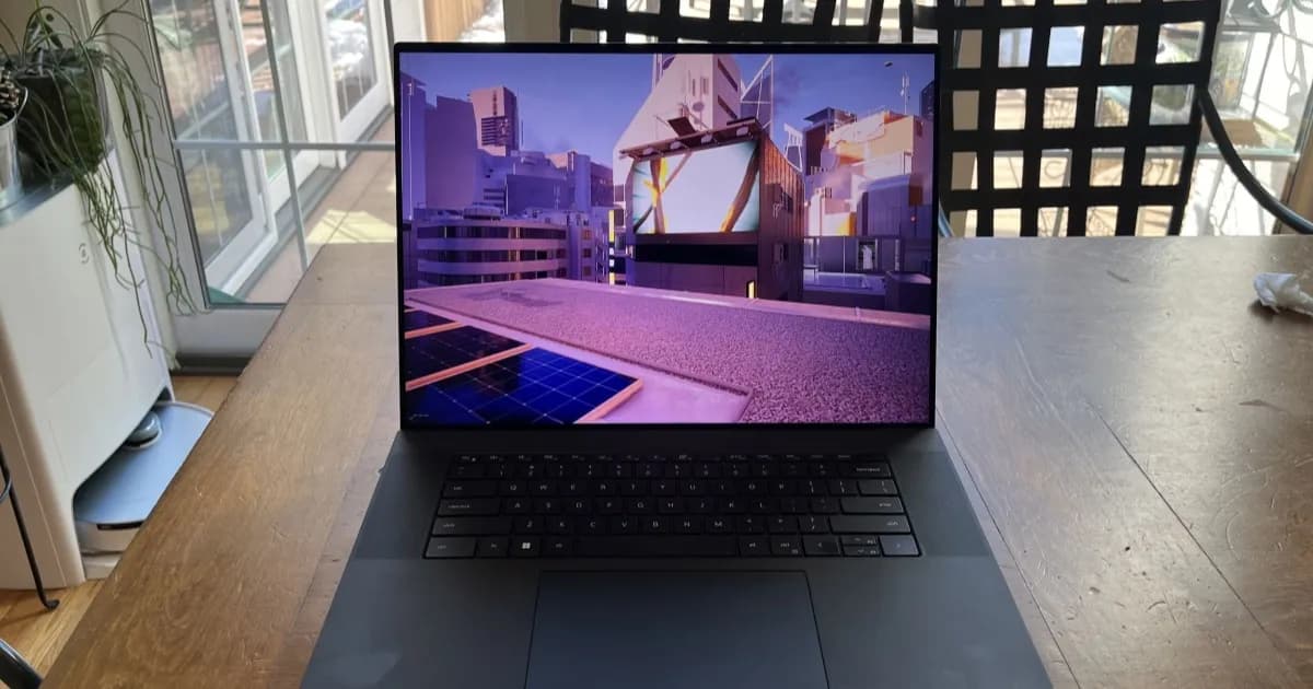 Laptop Dell XPS dengan layar menyala menampilkan logo Windows 11 di atas meja kayu