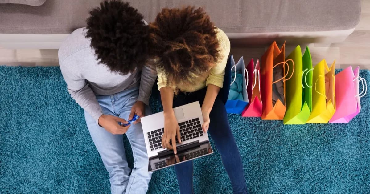 Ilustrasi konsumen berbelanja online dengan laptop dan berbagai tas belanja berwarna di sofa