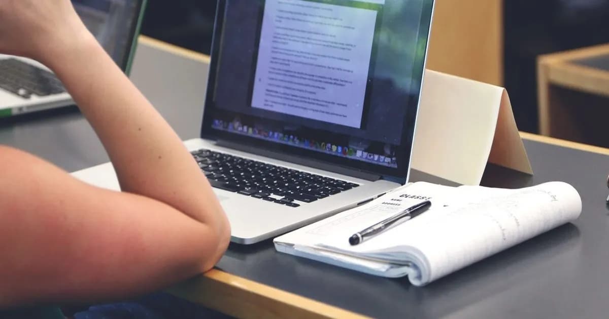 Mahasiswa mengetik di laptop di meja belajar dengan buku dan kalkulator