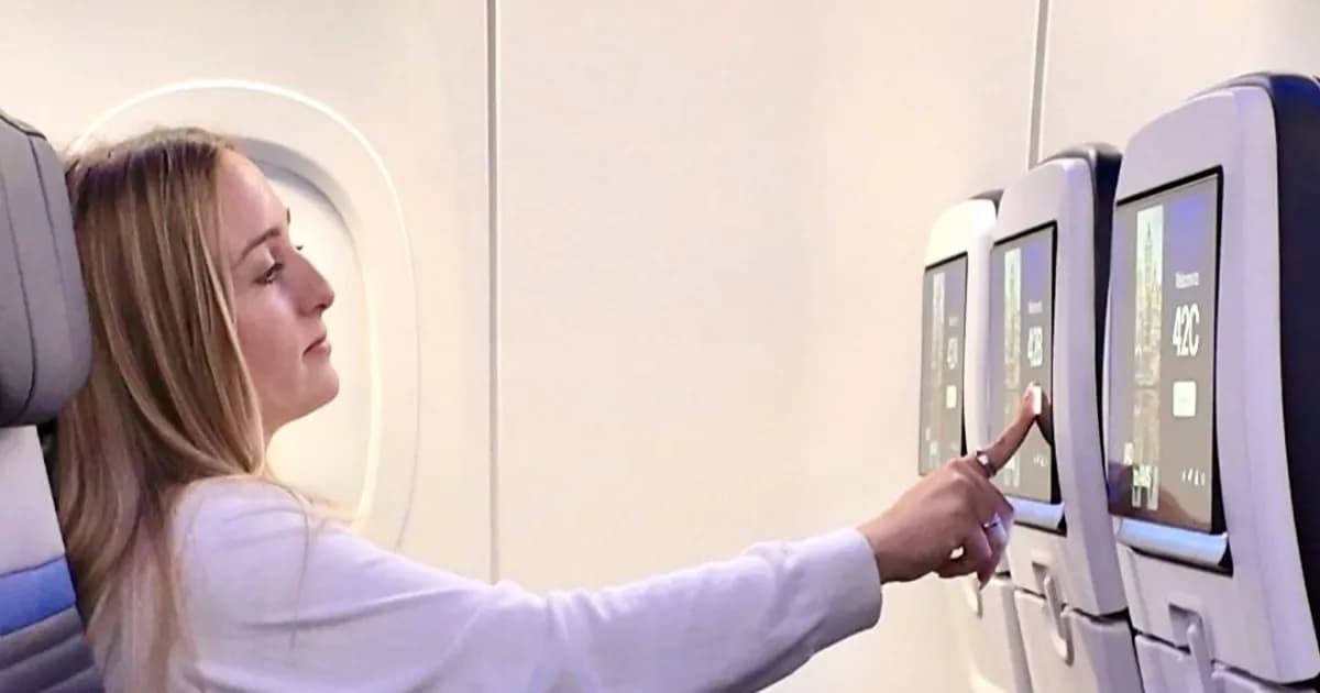 Penumpang wanita duduk di kursi kelas ekonomi United Airlines Airbus A321XLR sambil menyentuh layar OLED 4K di kursi pesawat