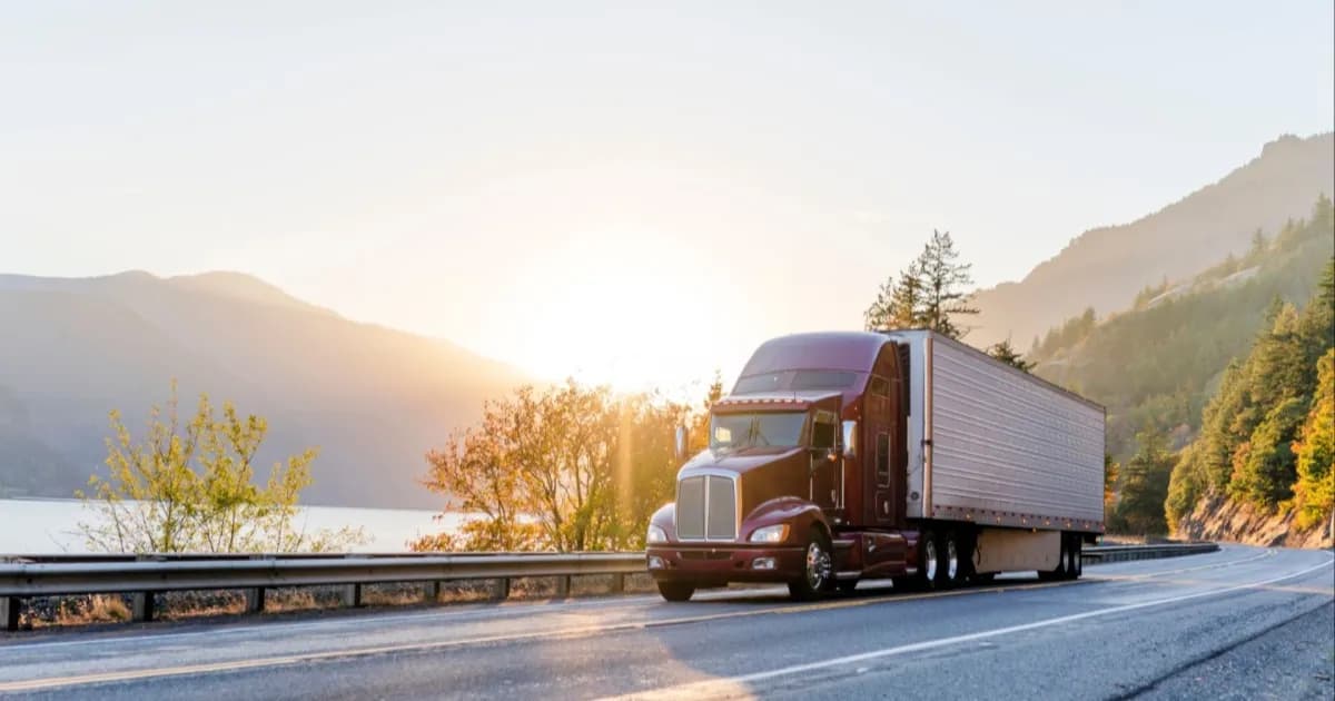 Truk semi coklat klasik Amerika yang kuat dengan trailer berpendingin mengangkut barang beku di jalan sepanjang sungai dan rel kereta di area Columbia Gorge dengan pegunungan