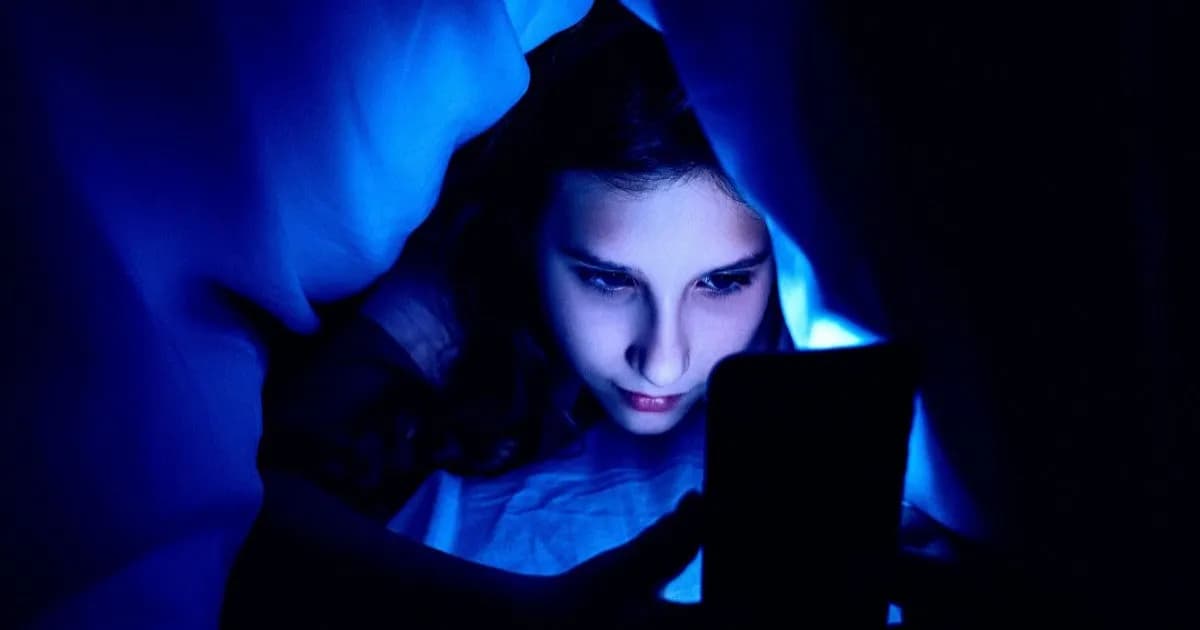 Seorang gadis melihat layar smartphone di bawah selimut, menggambarkan penggunaan AI oleh anak-anak.