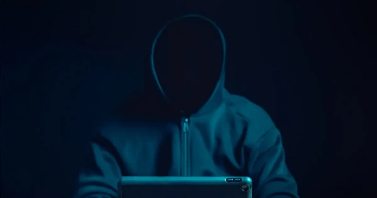 Ilustrasi sosok berjaket hoodie dengan wajah tersembunyi sedang menggunakan komputer, melambangkan identitas penulis palsu di internet.