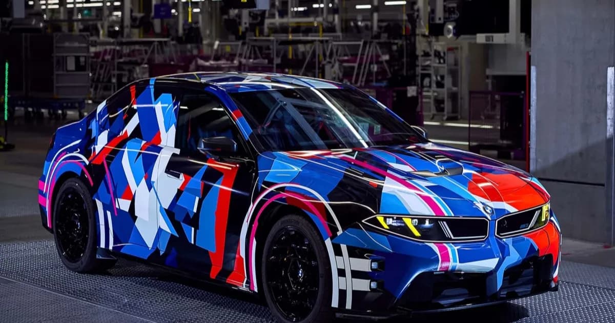 BMW M3 listrik dengan bodi produksi berkamuflase memperlihatkan lampu kuning khas dan lengkungan roda lebar