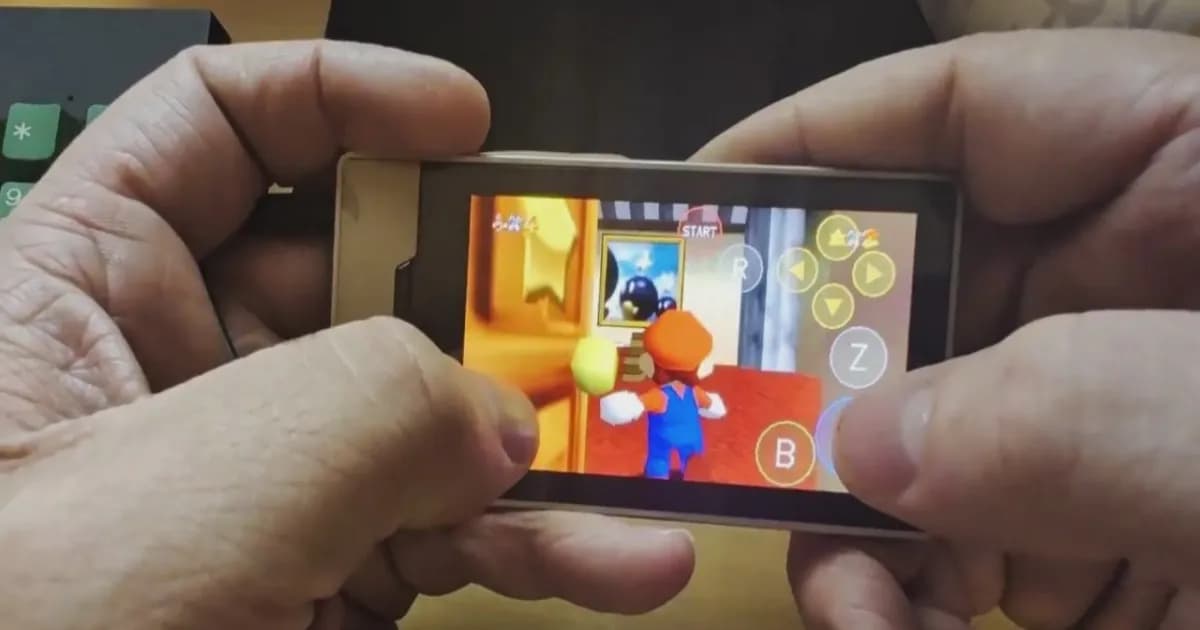Tangan memegang Zune HD dalam posisi menyamping dengan Super Mario 64 berjalan di layarnya, Mario berada di dalam kastil dan tombol sentuh tampil di sisi kanan
