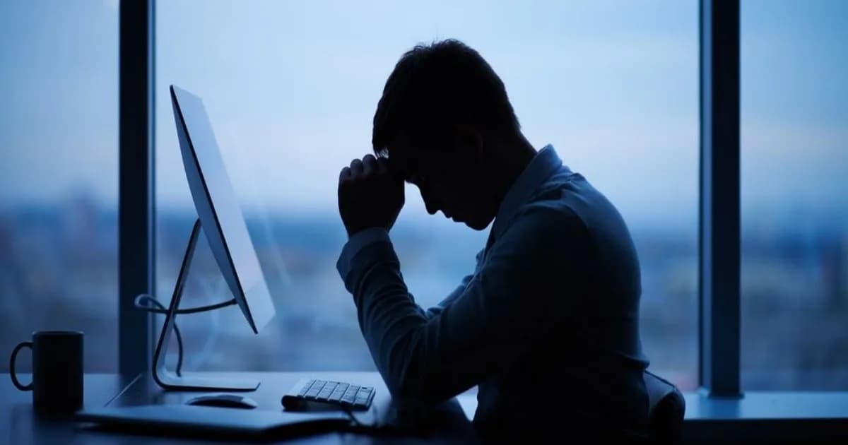 Karyawan bekerja dengan laptop di meja kerja yang menunjukkan ketidaknyamanan akibat perangkat teknologi kantor