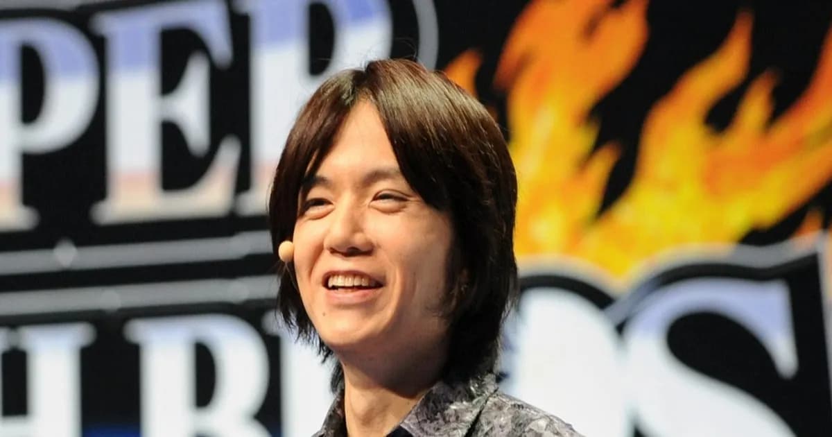 Masahiro Sakurai, kreator Super Smash Bros, dalam sebuah acara dengan banner Super Smash Brothers di belakangnya.