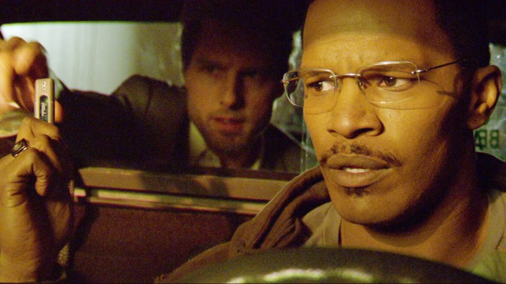 Tom Cruise sits in the back of a taxi with Jamie Foxx driving in Collateral.