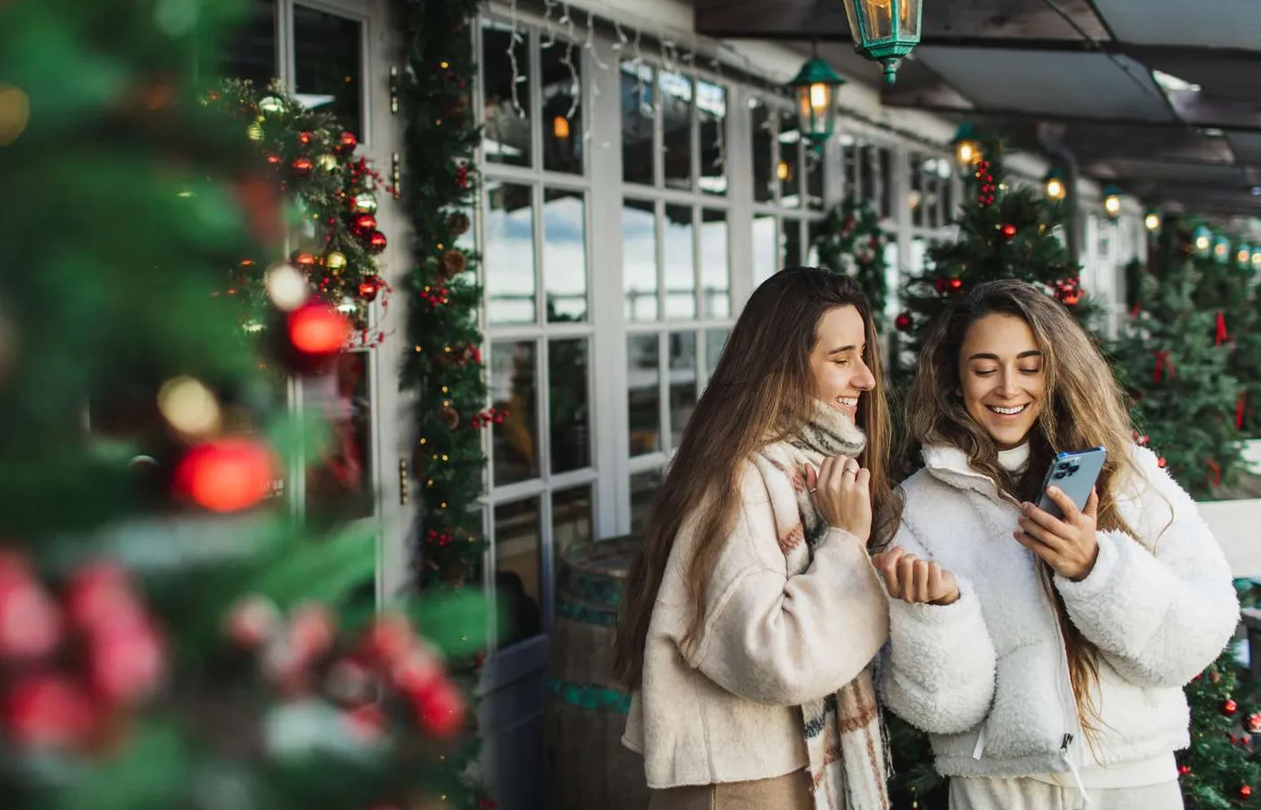 Dua orang tersenyum dan melihat smartphone di setting liburan outdoor dengan dekorasi Natal di sekitar