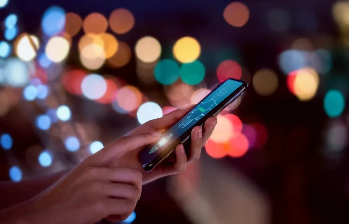 Orang menggunakan smartphone di malam hari dengan latar belakang lampu bokeh yang estetik